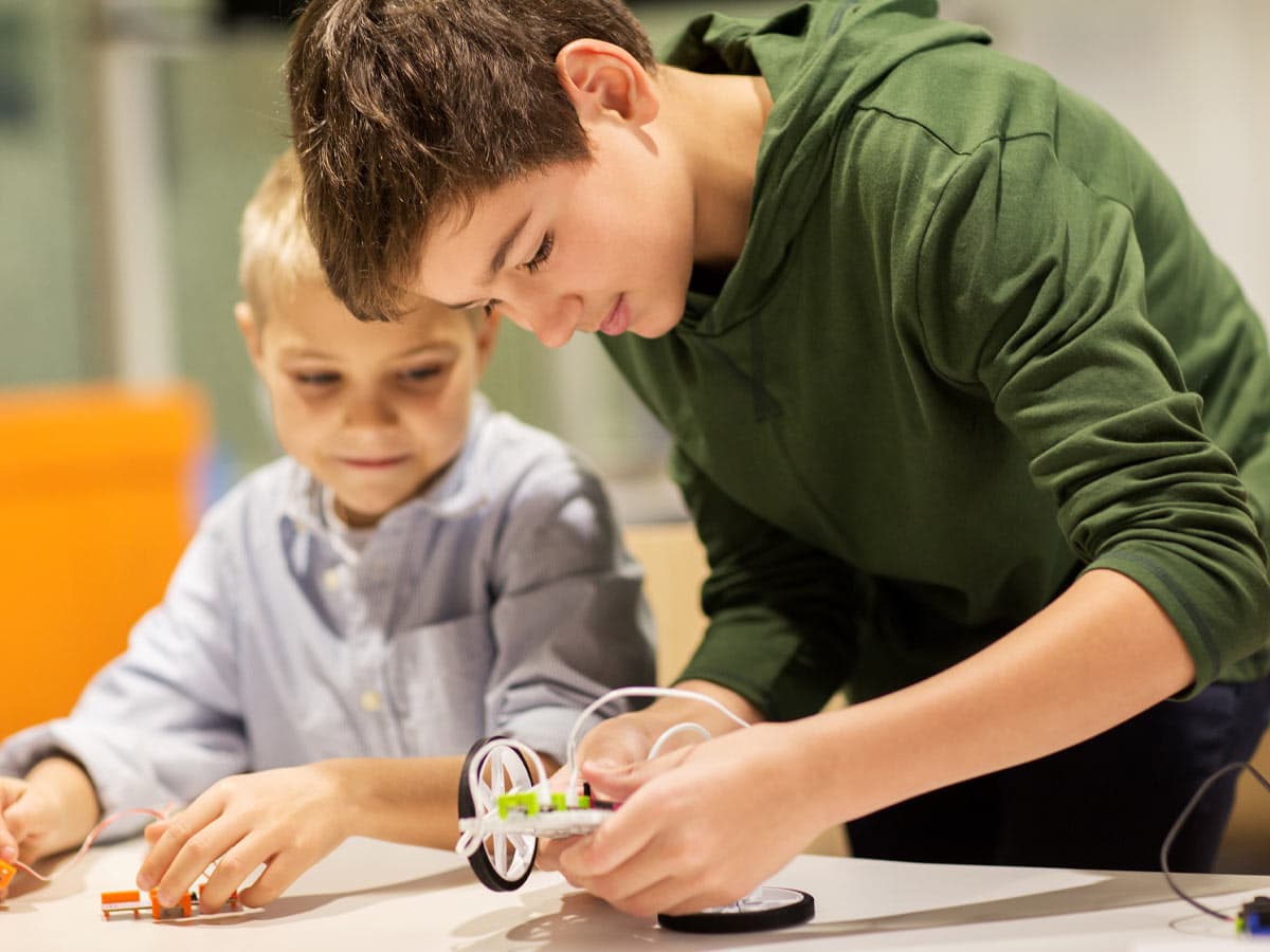Two boys sitting at a table building a small robot from an electronics kit
